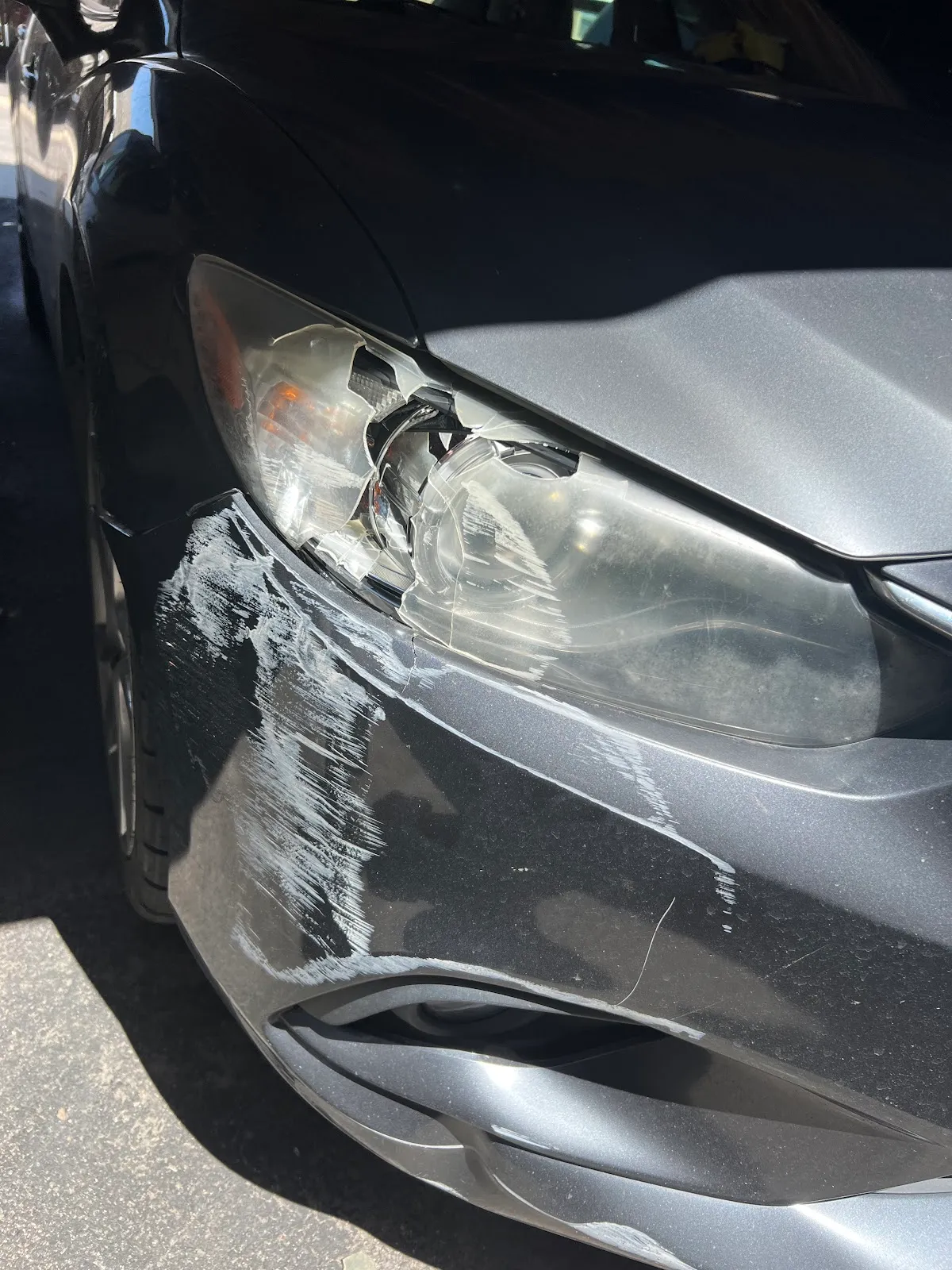 Front-end collision damage on a gray car: a cracked headlight and scraped front bumper, before repair